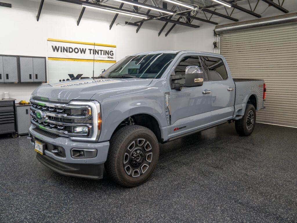 Gray pickup truck in a tint shop garage with a window tinting sign.
