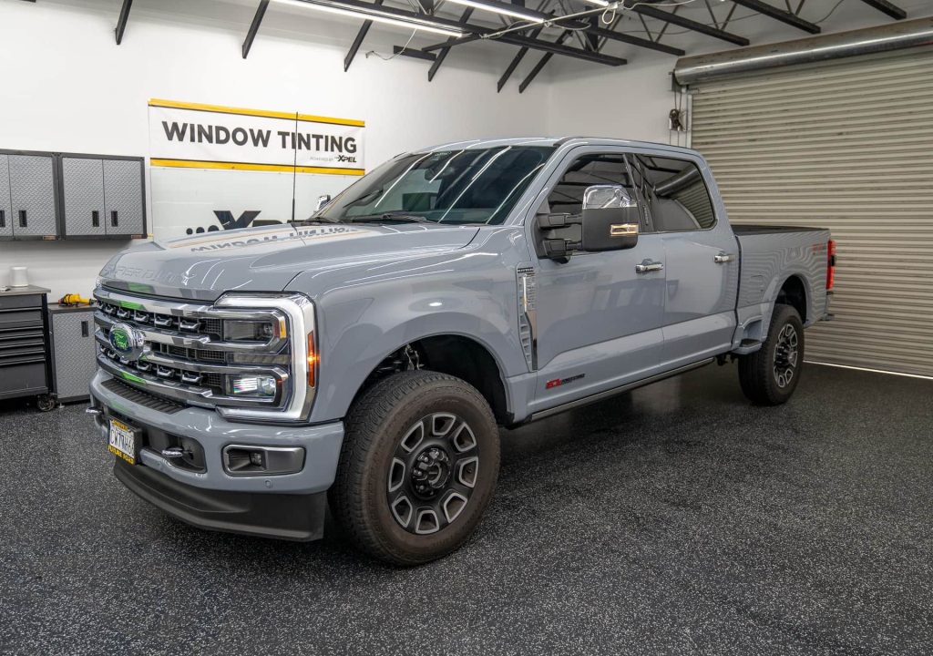 Gray pickup truck in a tint shop garage with a window tinting sign.